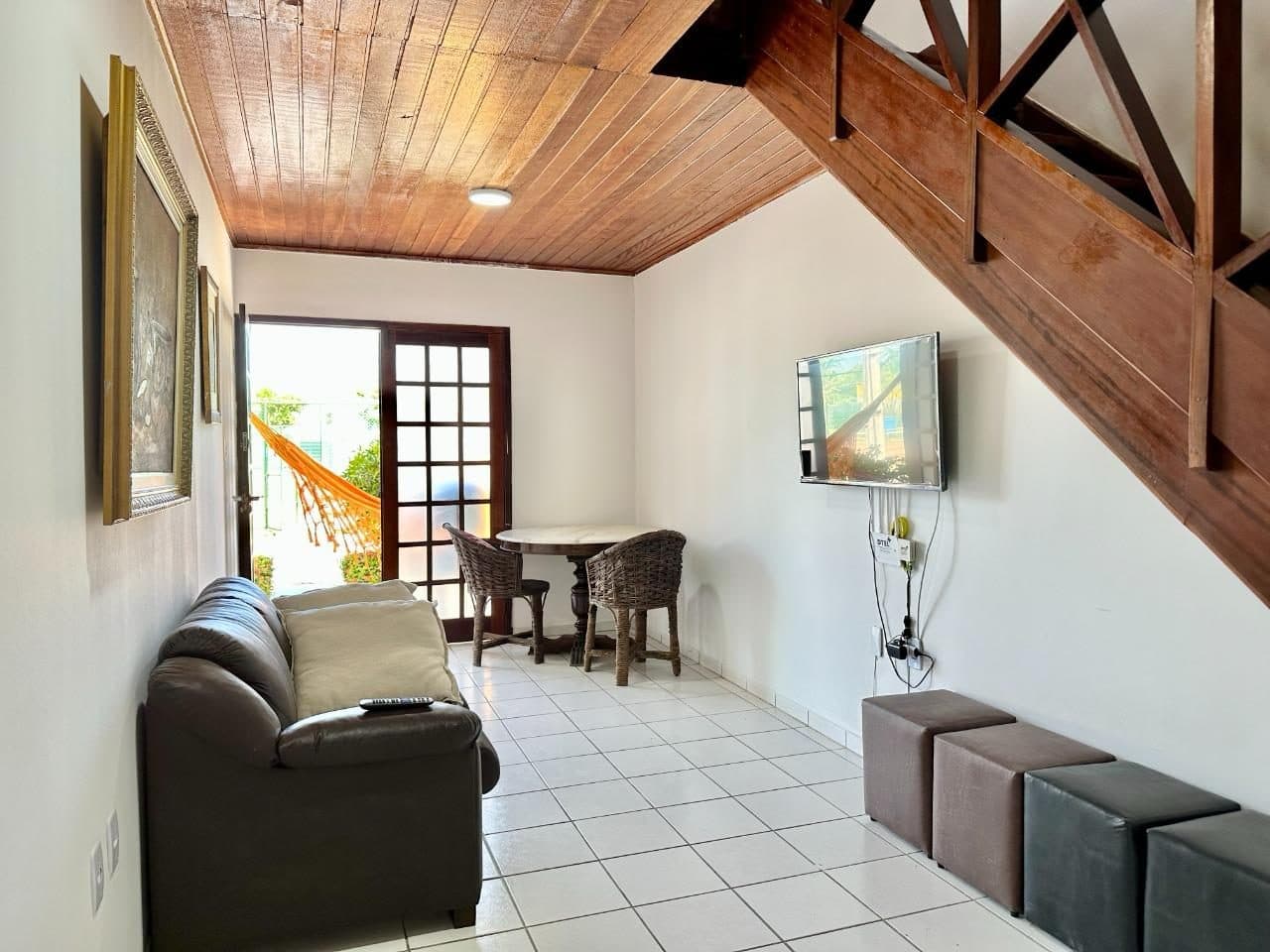 Sala com sofá, TV e mesa de jantar, com escada de madeira