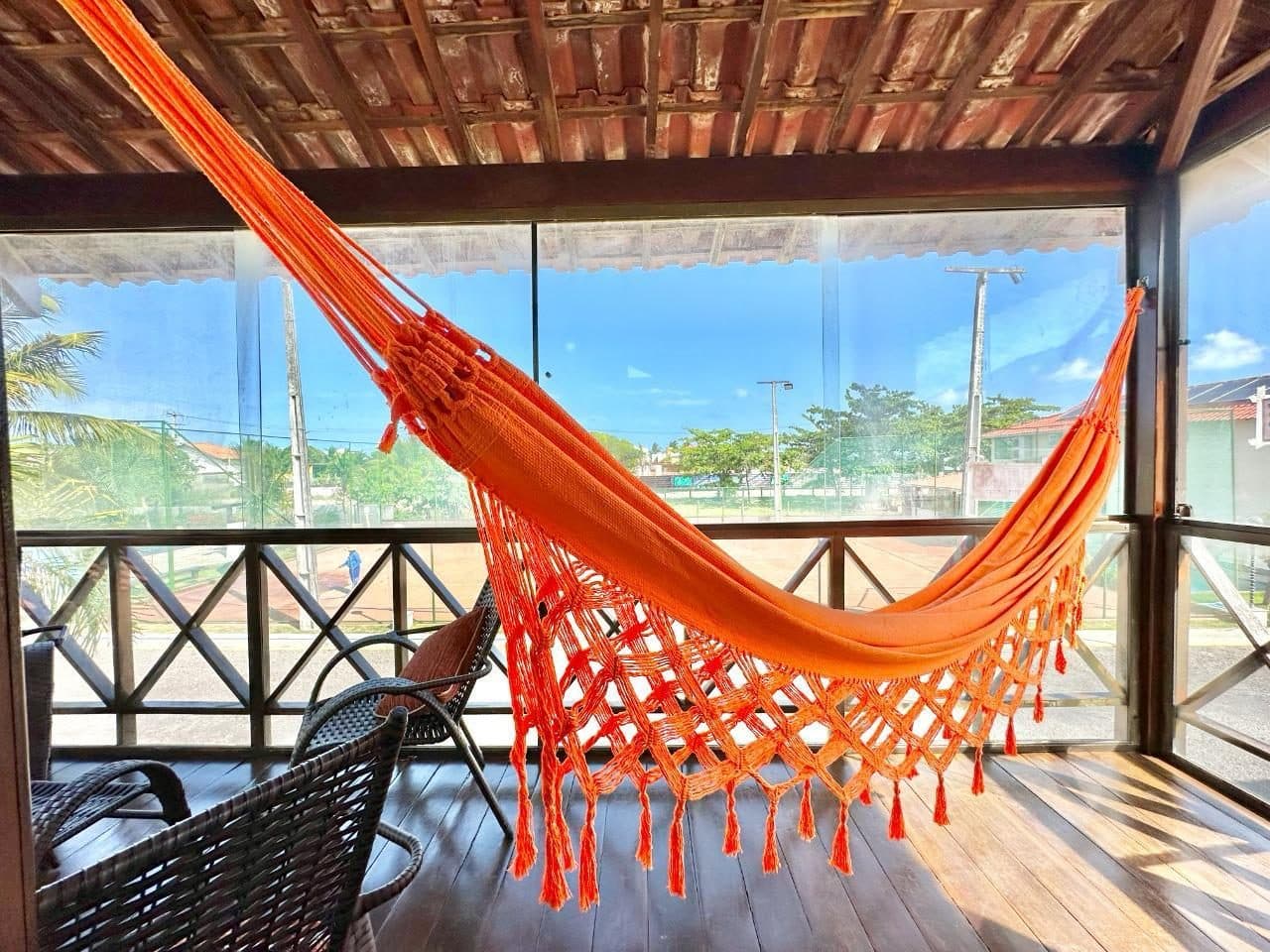 Varanda superior envidraçada com rede laranja e cadeiras